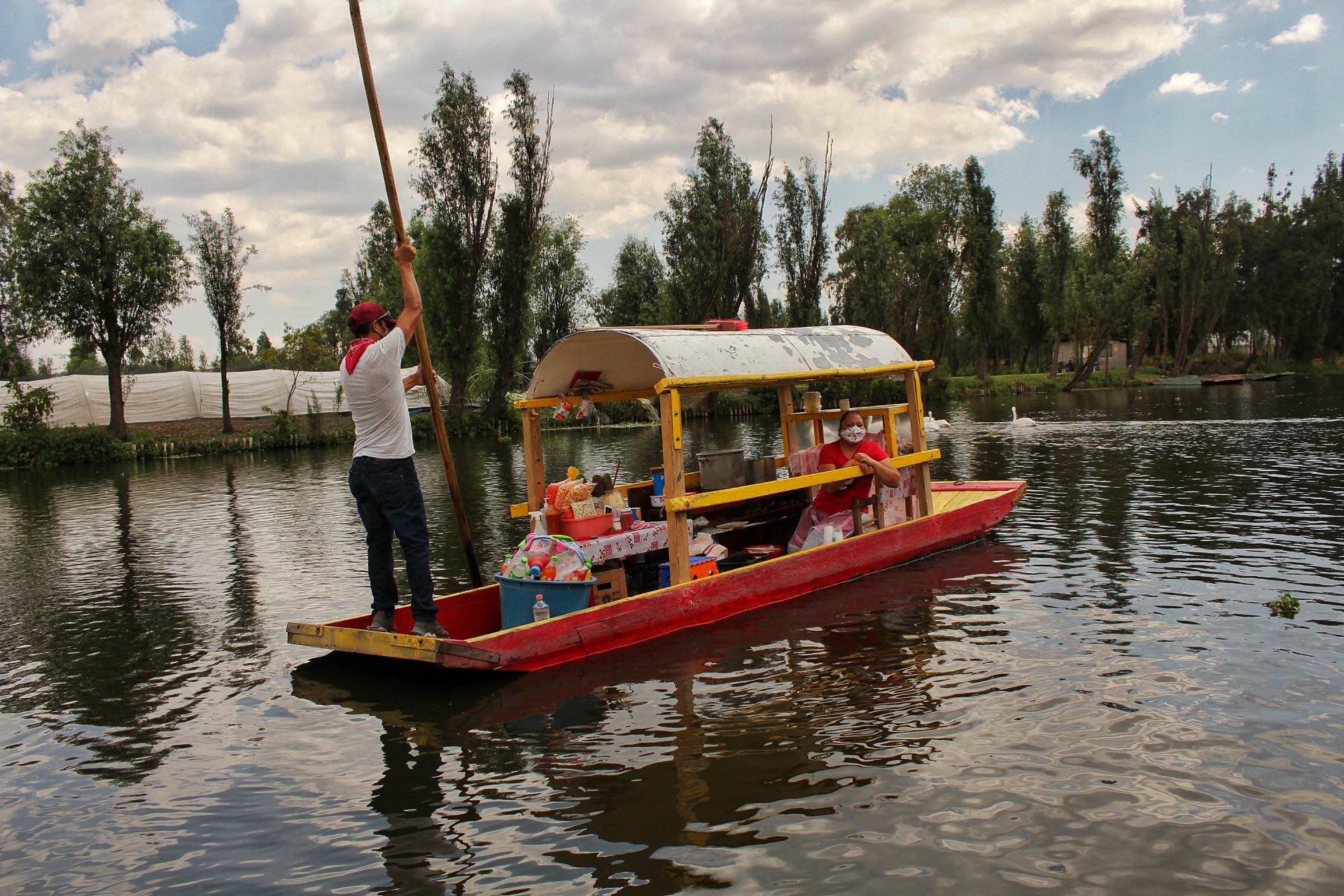 Trajinera roja y amarilla navegando por un canal de Xochimilco.